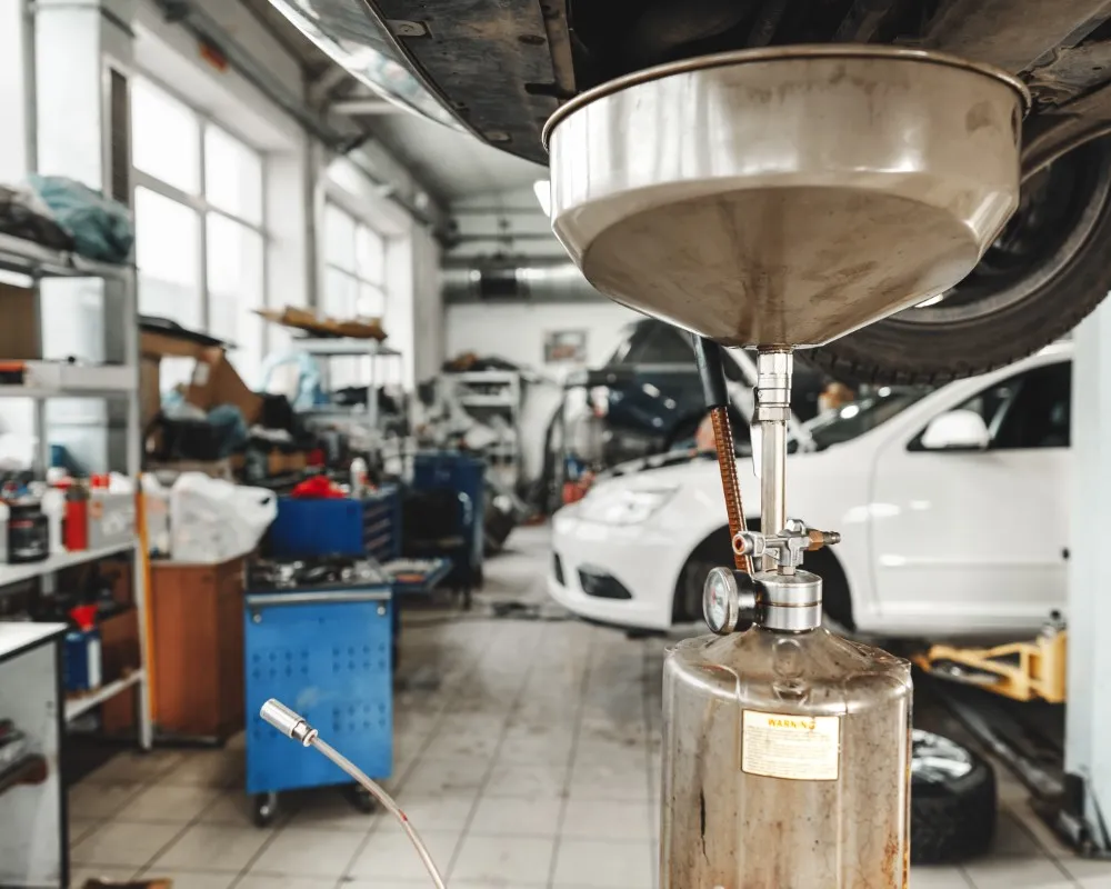 Used motor oil draining from the underside of a vehicle during an oil change to remove contaminants and prevent engine damage.