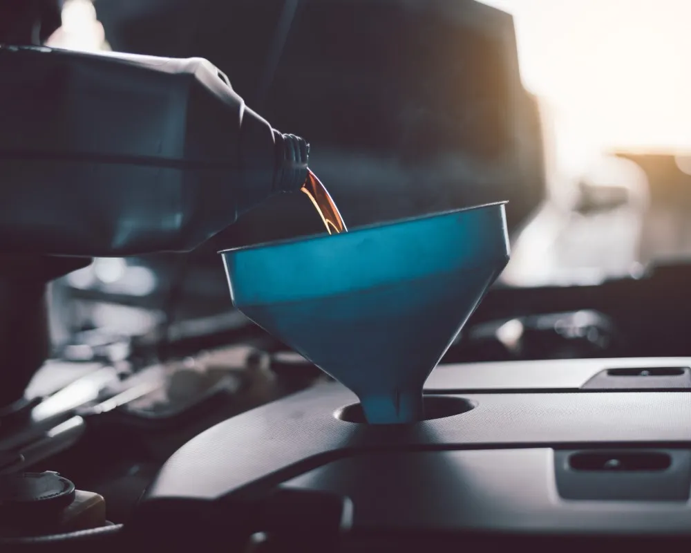 Fresh motor oil being carefully poured into a funnel as part of a routine oil change to maintain optimal engine performance.