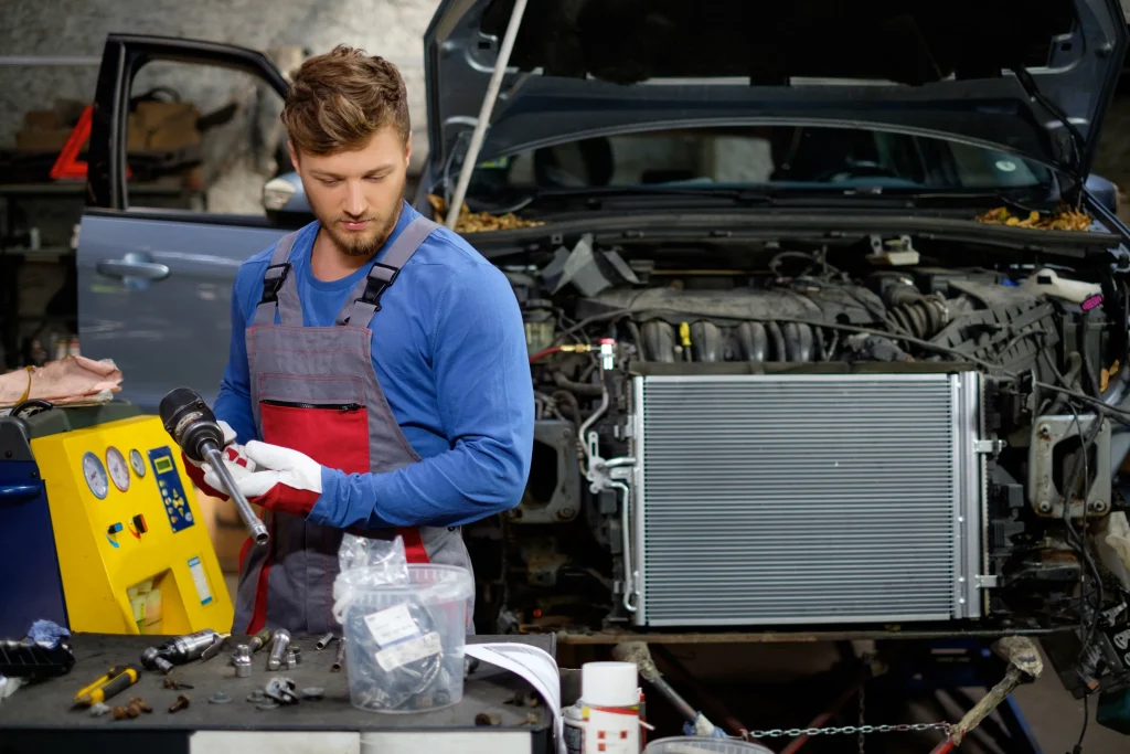 A focused auto mechanic in a professional workshop environment, preparing to perform radiator service on a car with the hood open, surrounded by tools and equipment.