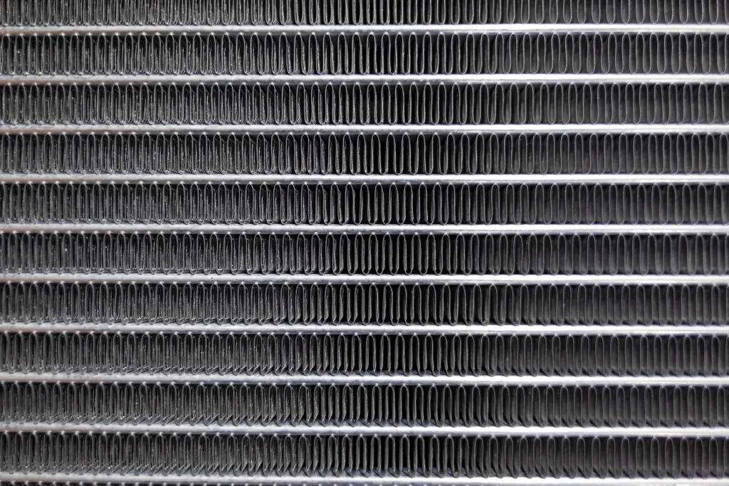 A detailed close-up view of the intricate fine fins and tubes of a car radiator, highlighting its critical components essential for efficient cooling and radiator service.