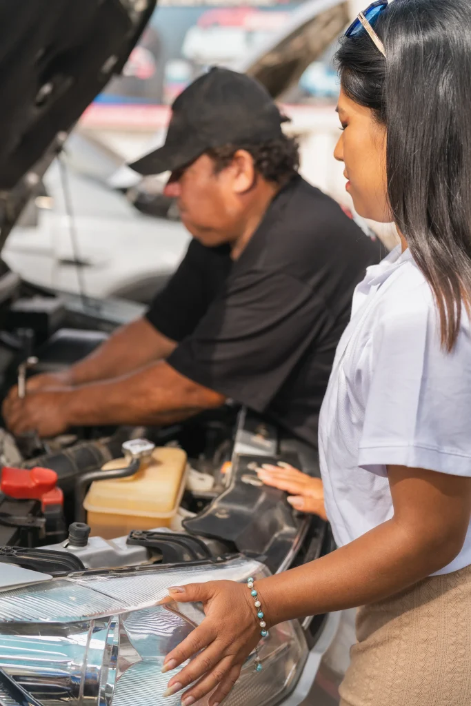 An expert mechanic performs car maintenance by checking the engine components under the hood for a female car owner.