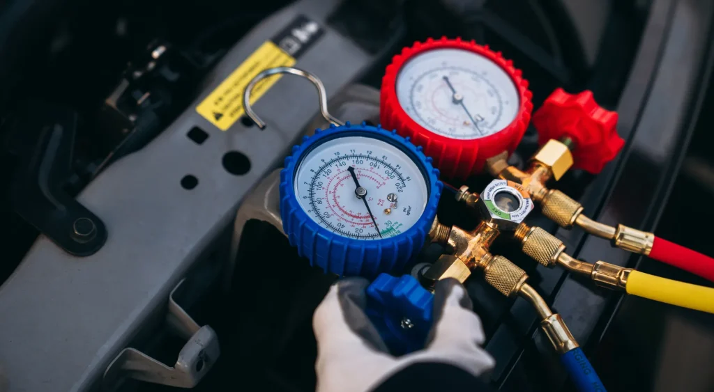 Mechanic performing a car air conditioning service using pressure gauges to check refrigerant levels.