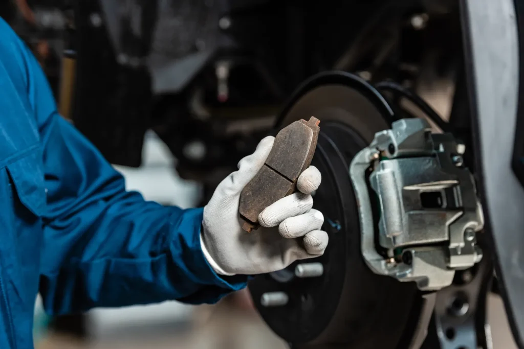 Mechanics holding an old brake pad during a car brake service in a repair shop.