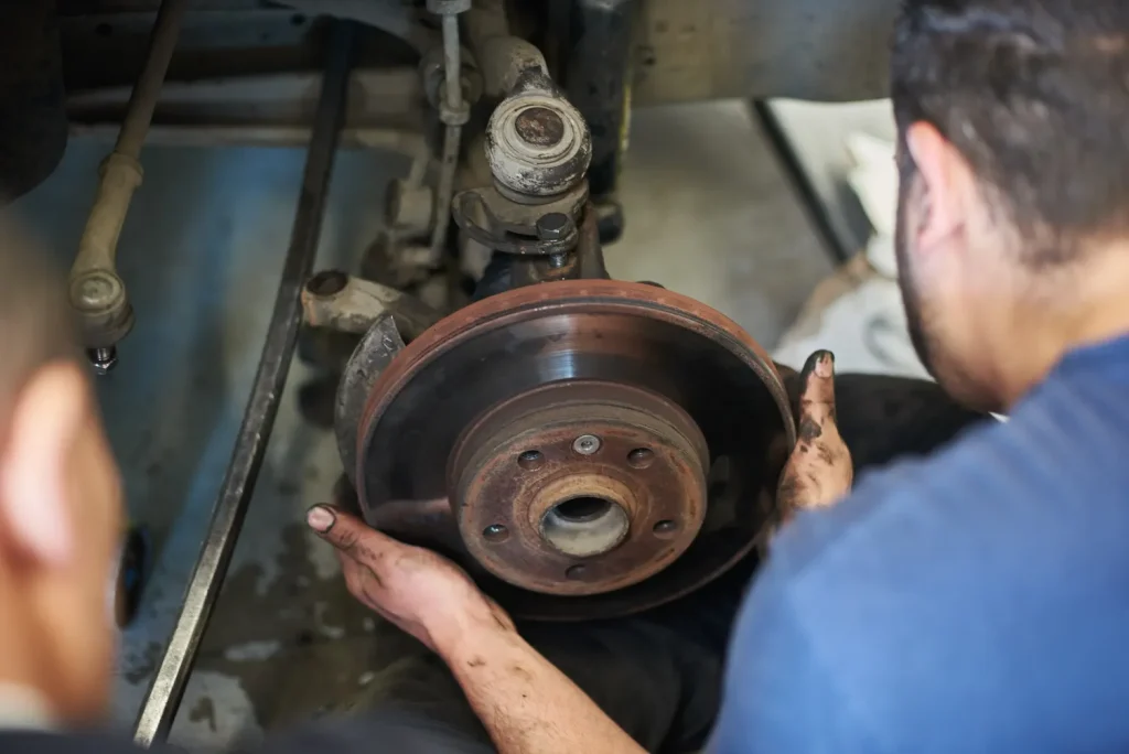 Mechanics hold a car's brake disc while another repairs it during a brake service.