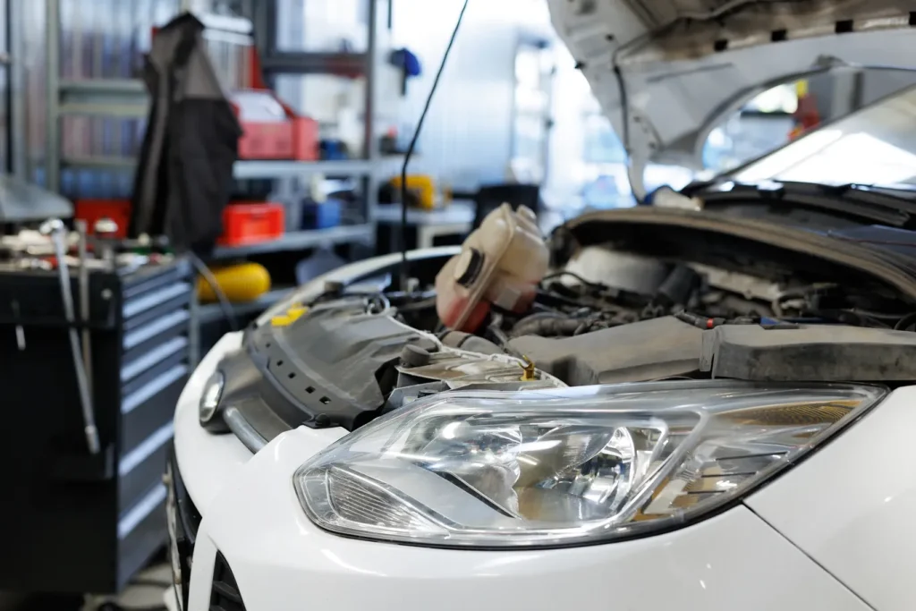 The open hood of a white modern car reveals the engine, awaiting a check-up, possibly an engine diagnostic service.