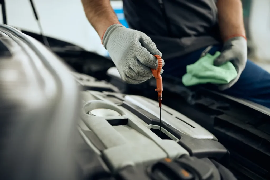Gloved hand holds up the oil dipstick, checking for clarity and proper level during an oil change process.