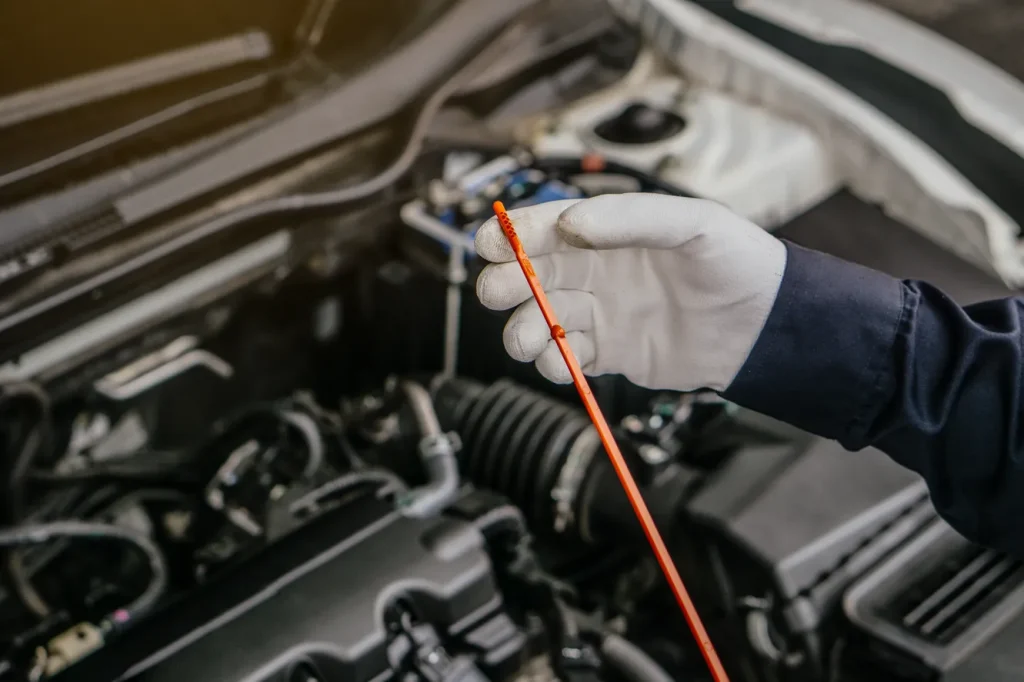 Mechanic checks car oil level with a dipstick during a routine oil change service in a garage.