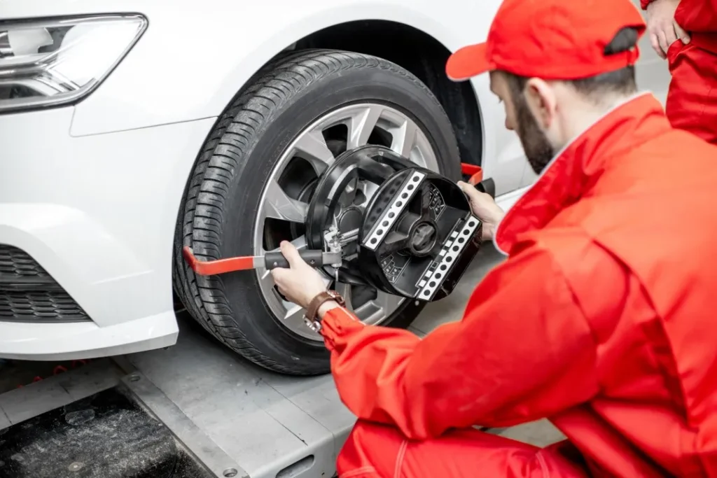 A professional auto mechanic in red uniform carefully adjusting the wheel alignment tool and sensors on a white car tire.