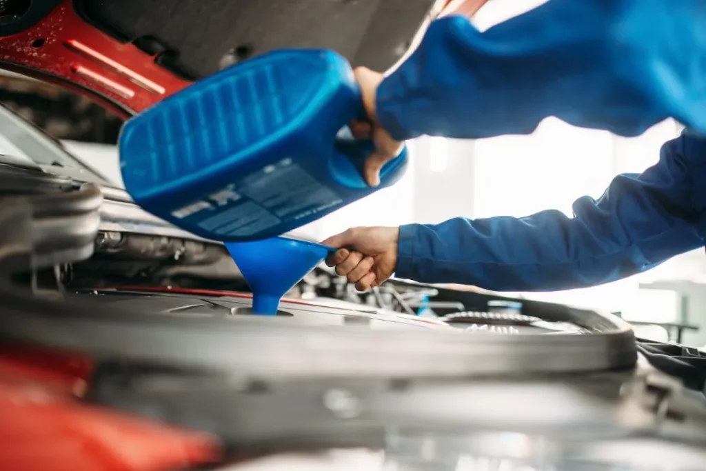 Blue jug pouring fluid into a car engine during a radiator service.