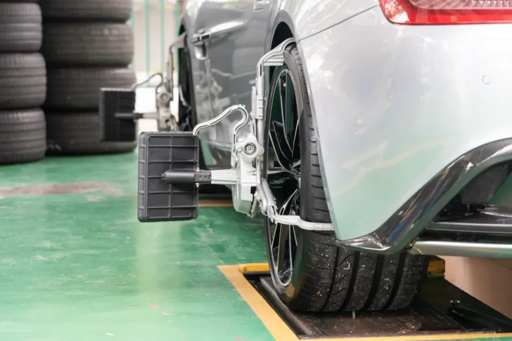 Rear wheel of a sleek car parked next to stacked tires, equipped with specialized calibration tools for a precise wheel alignment check.