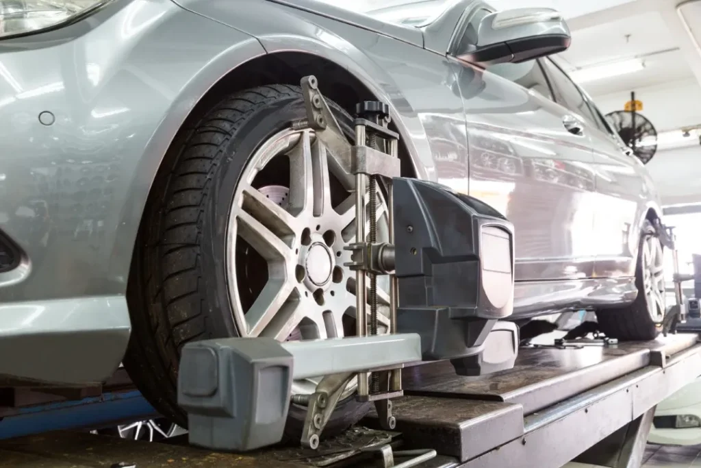 Silver car on a hydraulic lift undergoing a professional wheel alignment inspection with sensor equipment attached to the front tire.
