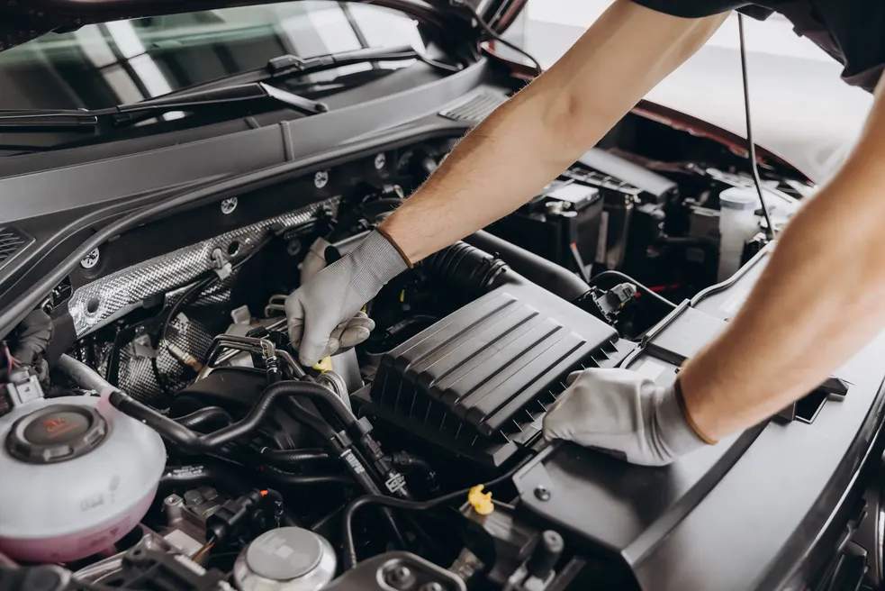 A close-up of a mechanic's gloved hands pointing at a specific engine part during a "car maintenance" inspection.