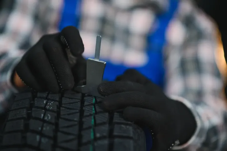 Manos con guantes negros midiendo la profundidad de la banda de rodadura con un calibrador de tire repair.