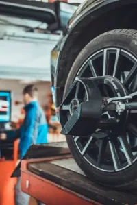 Wheel Alignment Close Up Of Car Tire With Alignment Tool Installed While Mechanic Works In Background Out Of Focus