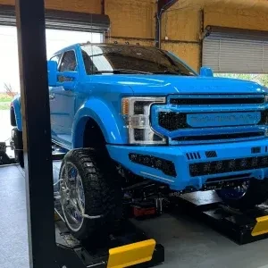 Custom light blue heavy duty pickup truck with large off road tires being serviced on a professional garage lift
