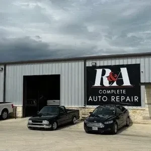 The front of a modern metal auto repair shop featuring large signage and various customer vehicles in the lot