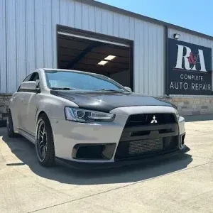 Modified silver Mitsubishi sports car with black aftermarket wheels outside a professional automotive garage