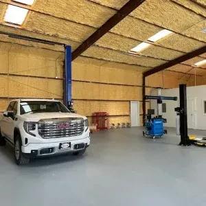 A new white GMC truck sitting on a polished grey floor next to professional blue and black vehicle lift posts