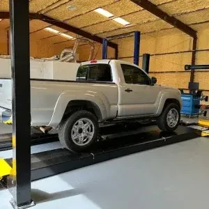A silver Toyota Tacoma truck positioned on a black automotive lift system for maintenance in a clean repair shop