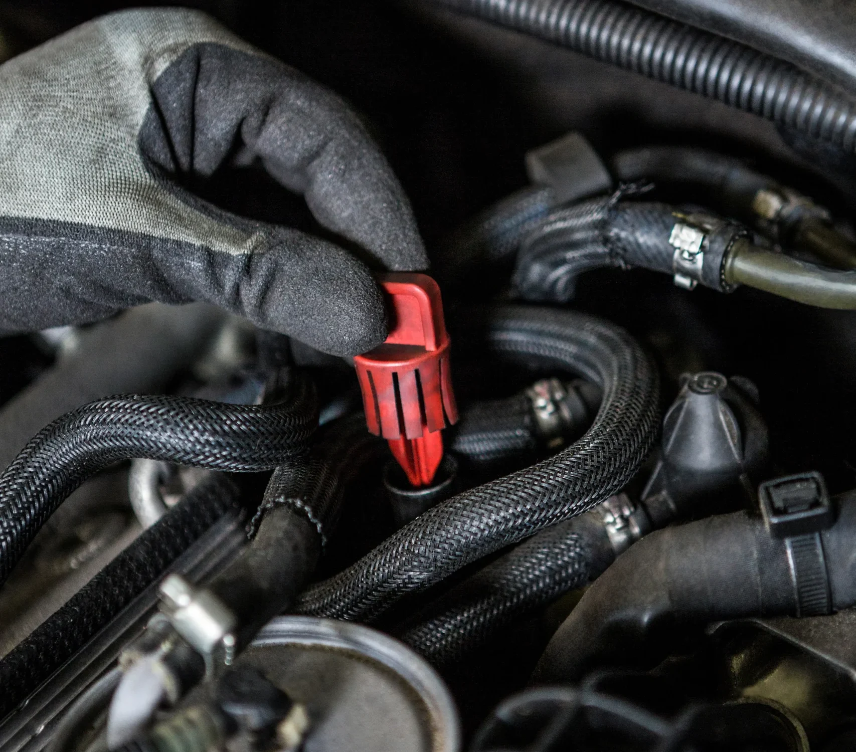 Mecánico realizando la reparación de alternadores al revisar las conexiones y el cableado del sistema eléctrico en el compartimento del motor.