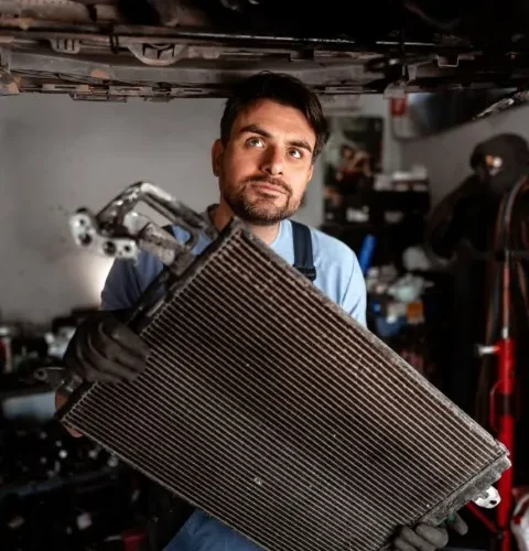 Mechanic holding a dirty, old car radiator after removal for service.